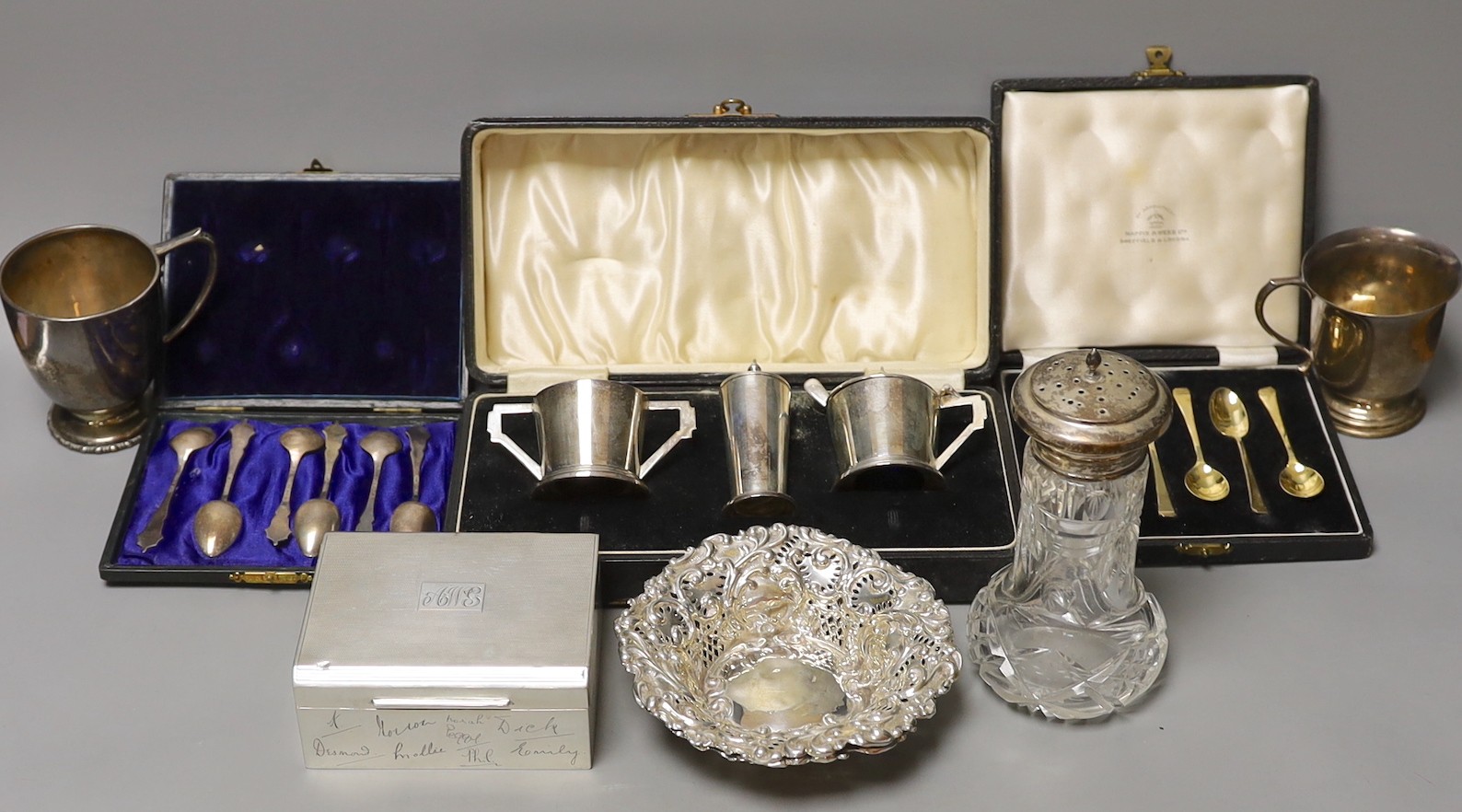 A group of mixed silver, including a cigarette box, two silver christening mugs, two similar pierced bonbon dishes, a cased Art Deco three piece condiment set, two cased sets of six teaspoons one enamelled stamped sterli